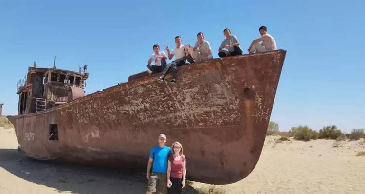 Bezoekers die klimmen en poseren op een roestend schip gestrand op de woestijnzanden van de scheepsbegraafplaats van het Aralmeer.
