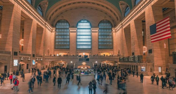 Grand hall d'une gare ferroviaire ornée grouillante de voyageurs.