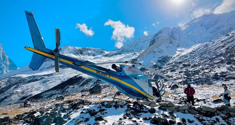 Hélicoptère incliné sur des rochers enneigés sous un soleil alpin éclatant avec des randonneurs à proximité