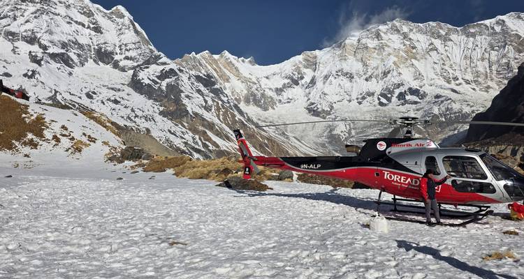 Hélicoptère rouge attend sur un champ enneigé au camp de base de l'Annapurna entouré de sommets