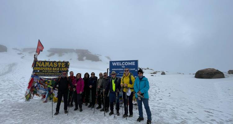 Groupe de randonneurs posent près du panneau Bienvenue au camp de base de l'Annapurna au milieu du brouillard et de la neige