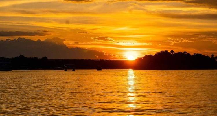 Goldene Sonne, die über einem breiten, ruhigen Fluss untergeht und Spiegelungen über das Wasser wirft.