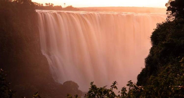 Die Victoriafälle stürzen in einem mächtigen Wasservorhang herab, der in warmes Abendlicht getaucht ist.