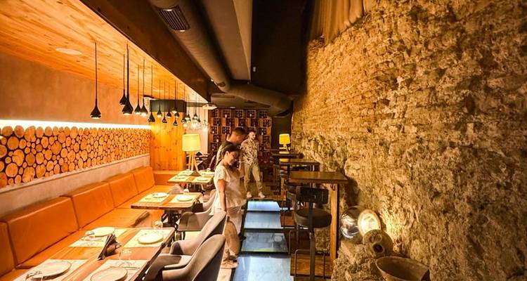 Warm beleuchtetes modernes Restaurant-Interieur mit Steinwand und zwei Gästen, die einen Glasbodenbereich betrachten