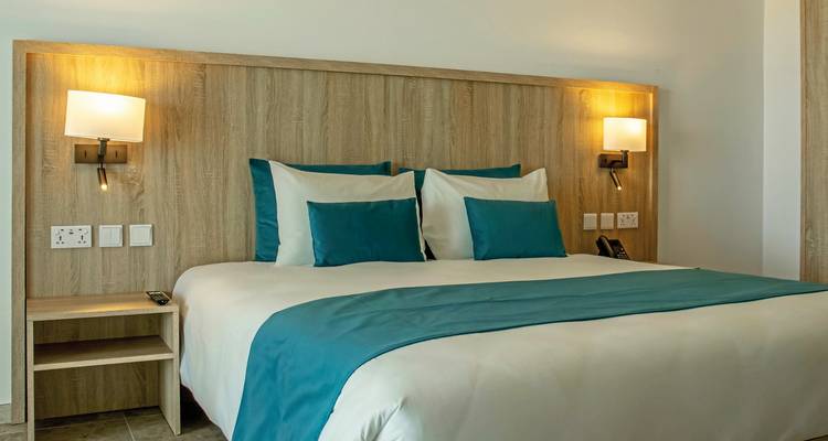 Einfaches Hotelschlafzimmer mit Holzkopfteil und türkisfarbenen Kissen, beleuchtet von warmen Nachttischlampen.