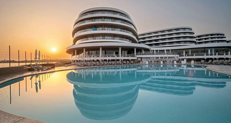 Sonnenuntergangsschein spiegelt sich in einem großen Außenpool neben einem modernen terrassenförmigen Hotelkomplex wider.