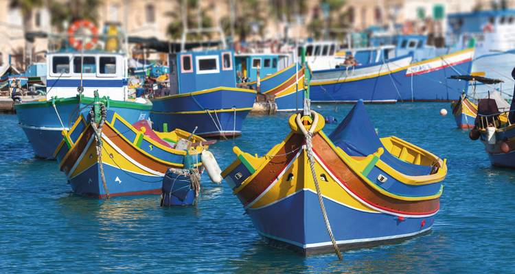 Primer plano de botes luzzu malteses pintados de colores brillantes con motivos de ojos flotando en agua azul.