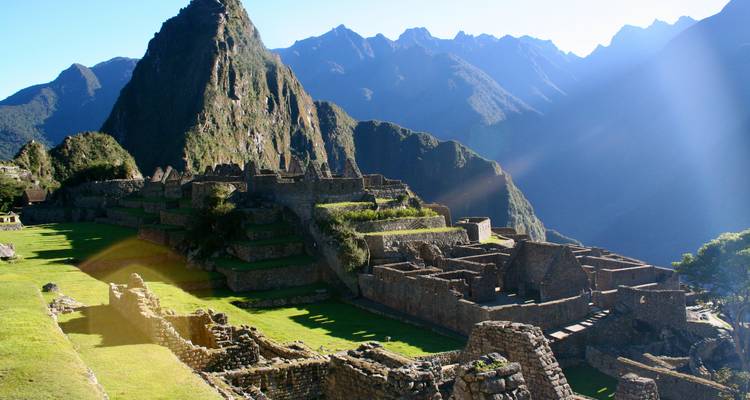 Sweeping sunrise view of Machu Picchu's stone terraces with Huayna Picchu peak and misty Andes behind.