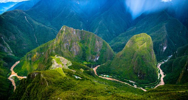Aerial perspective of lush mountains surrounding the winding river and distant Inca ruins near Machu Picchu.