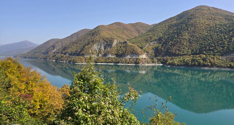 Kalm turquoise reservoir weerkaatst beboste heuvelflanken met herfstkleuren in Georgia.