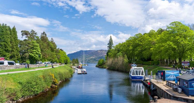 Canal calédonien avec bateaux amarrés menant vers des collines boisées sous un ciel bleu