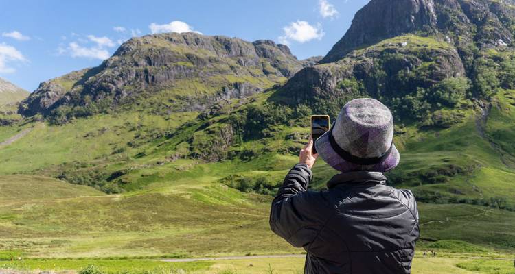 Touriste en chapeau prend une photo mobile des falaises vertes dans les Highlands par une journée ensoleillée