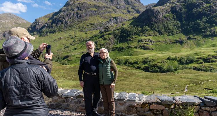 Des voyageurs prennent la pose pour une photo devant les pentes vertes spectaculaires de Glencoe tandis qu'un autre prend une photo.