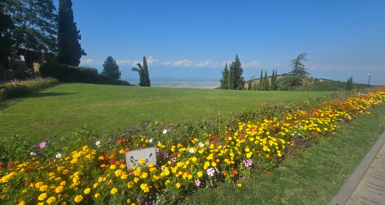 Gepflegter Rasen, gesäumt von bunten Blumenbeeten, überblickt ein fernes Tal und blauen Himmel in Kachetien, Georgien.