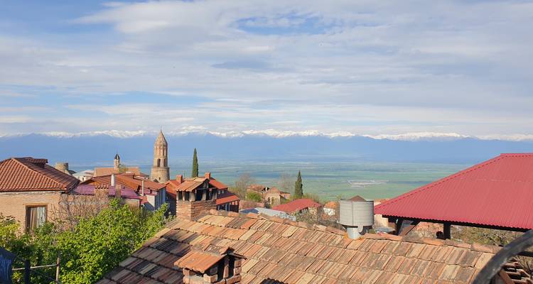 Dächer der Altstadt von Sighnaghi mit Kirchturm, der die fernen schneebedeckten Kaukasus-Berge einrahmt.