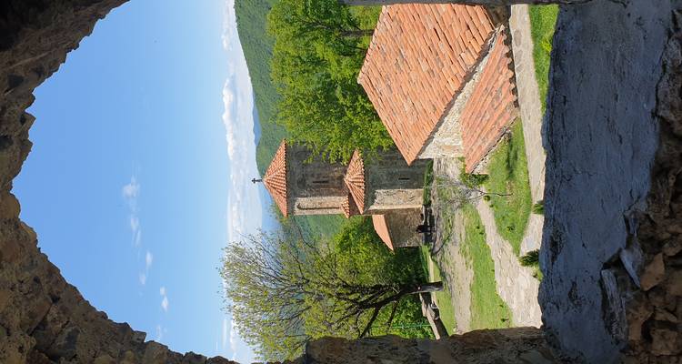 Ein Steinbogen rahmt eine rustikale Bergkuppe-Kirche mit Terrakotta-Dächern inmitten üppiger bewaldeter Hügel ein.