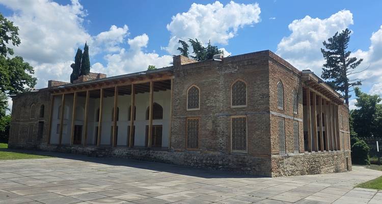 Historischer Backsteinpalast mit gewölbten Fenstern und hölzerner Kolonnade unter einem strahlend blauen georgischen Himmel.