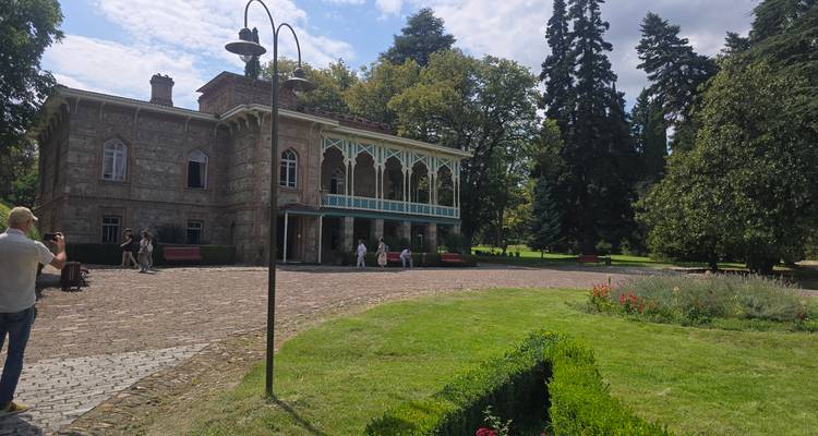 Elegantes Herrenhaus aus dem 19. Jahrhundert mit verziertem Balkon inmitten gepflegter Gärten und hoher Bäume.