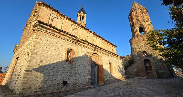 Steinkirche und hoher Glockenturm vor klarem blauen Himmel in Georgiens Weinregion.