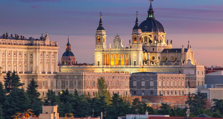 De verlichte Almudena Kathedraal en het Koninklijk Paleis van Madrid gloeien in de schemering tegen een kleurrijke hemel.