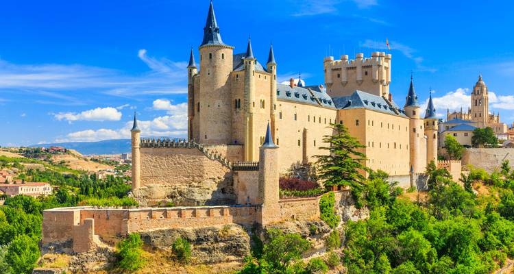 Het sprookjesachtige Alcázar van Segovia rijst op boven een beboste klif onder een heldere blauwe hemel.