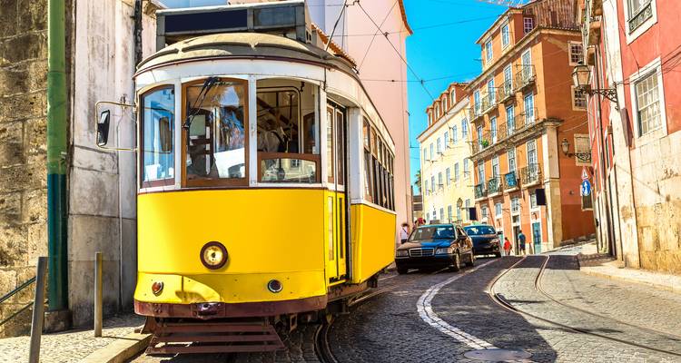 Close-up van Lissabons iconische gele tram die door een geplaveide straat navigeert op een zonnige dag.