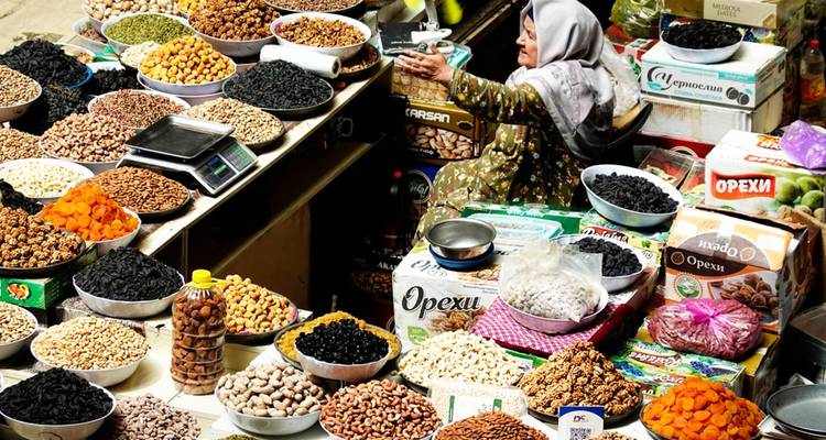 Une femme âgée vend un assortiment de fruits secs et de noix dans un étal de marché couvert animé.