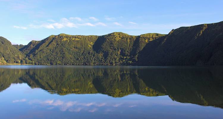 Lago cristalino reflejando perfectamente acantilados verdes bajo el cielo azul en Sete Cidades.