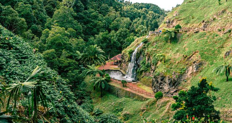 Valle verde con pequeña cascada junto a una terraza y palmeras en las colinas de las Azores
