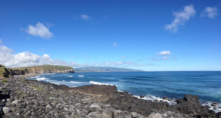 Orilla rocosa de basalto con olas ondulantes bajo un cielo azul brillante