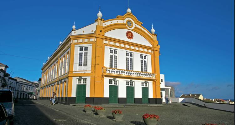 Edificio teatral neoclásico amarillo brillante y blanco en una calle empedrada bajo cielos despejados