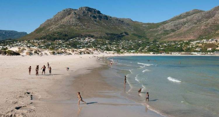 Les familles profitent d'une large plage de sable avec des montagnes et une ville côtière en toile de fond près du Cap.