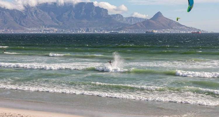 Un kitesurfeur éclabousse dans les vagues avec l'emblématique Table Mountain et Lion's Head à l'horizon.