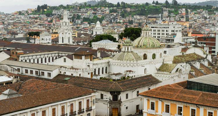 Vue aérienne du centre historique de Quito avec des dômes blancs ornés et un paysage urbain s'étendant dans les collines.
