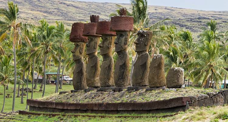 Icónica fila de estatuas moai con sombreros pukao entre palmeras en la Isla de Pascua.