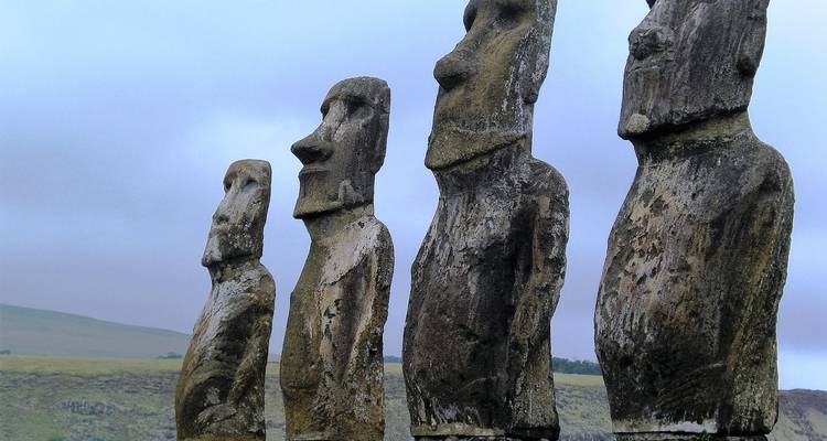 Vista angular de primer plano de cuatro estatuas moai desgastadas contra un cielo gris.