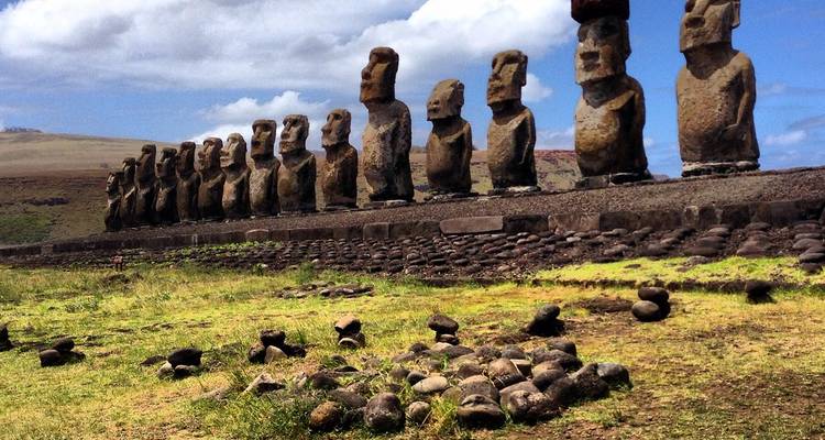 Larga fila de estatuas moai extendiéndose hacia la distancia sobre plataforma cubierta de hierba bajo cielo parcialmente nublado.