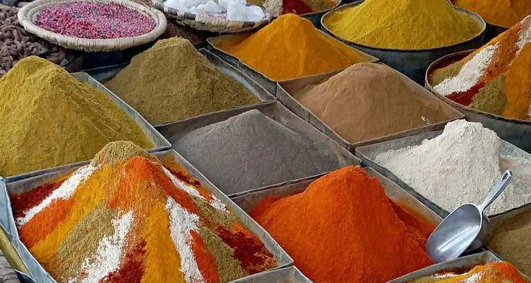 Des pyramides colorées d'épices soigneusement disposées dans des plateaux métalliques sur un marché marocain animé.