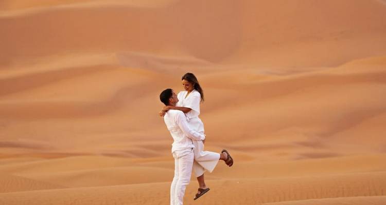 Couple vêtu de blanc s'enlace de manière ludique au milieu de vastes dunes de sable ondulantes.