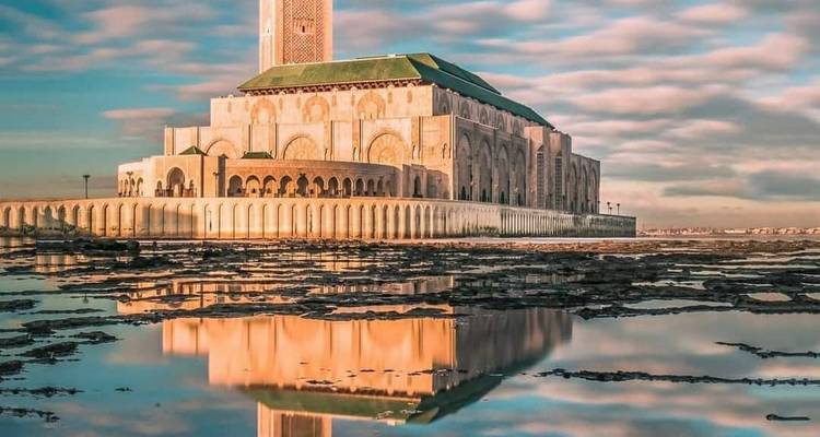 La Mosquée Hassan II se reflétant dans des bassins de marée calmes sous des nuages pastel au lever du soleil à Casablanca.