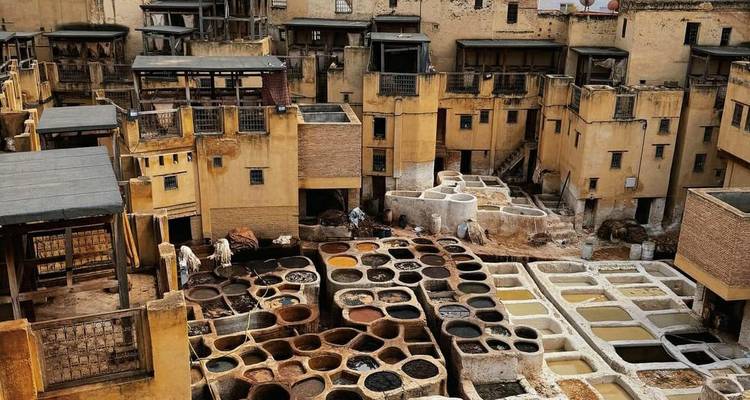 Vue panoramique des tanneries de Fès avec des cuves en nid d'abeille de teintures au milieu de bâtiments médiévaux jaunis.