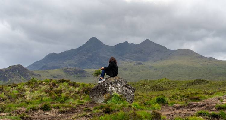 Un voyageur solitaire est assis sur un rocher contemplant les pics déchiquetés de l'île de Skye.