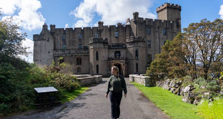 Un visiteur se promène vers les murs de pierre et les tours du château de Dunvegan sous un ciel lumineux.