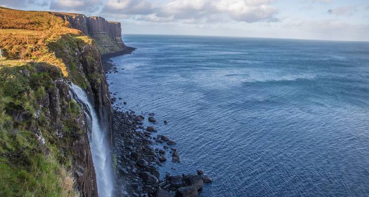 Une haute cascade plonge des falaises abruptes dans les eaux bleues le long de la côte sauvage de l'Écosse.