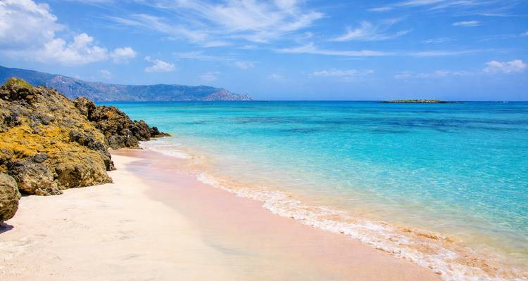 Idyllic Elafonisi beach with pink-tinged sand, clear turquoise water and distant mountains.