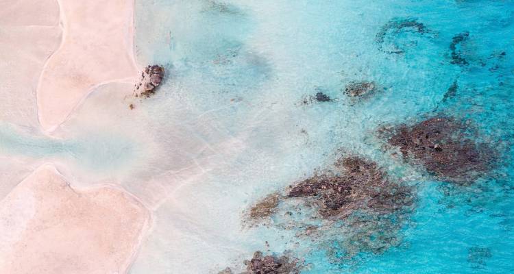 Abstract aerial view of shallow turquoise lagoon and pale sandbars with coral patches.