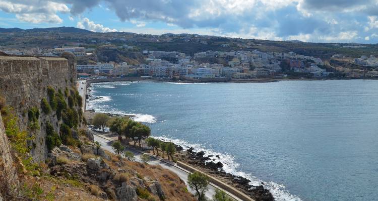 Coastal cityscape of Rethymnon viewed from fortress walls with shimmering bay below.