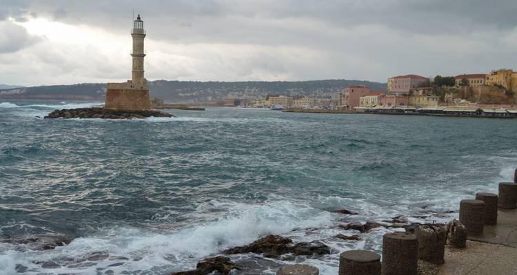 Rough seas crash near the Chania lighthouse with the old town visible across the bay.
