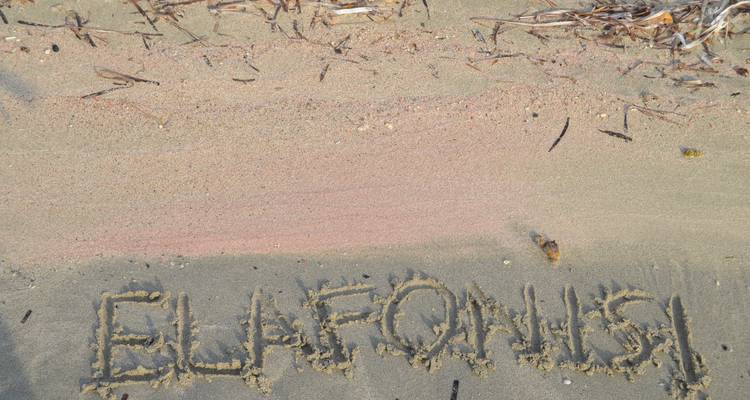 Zandstrand met het woord 'ELAFONISI' in het zand geschreven naast een strook roze zandkorrels.