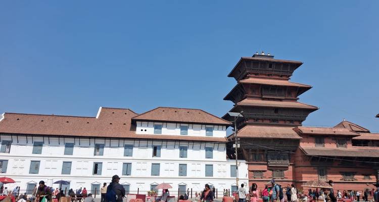 Wide shot of Kathmandu Durbar Square highlighting contrasting white and red palace buildings against clear blue sky.